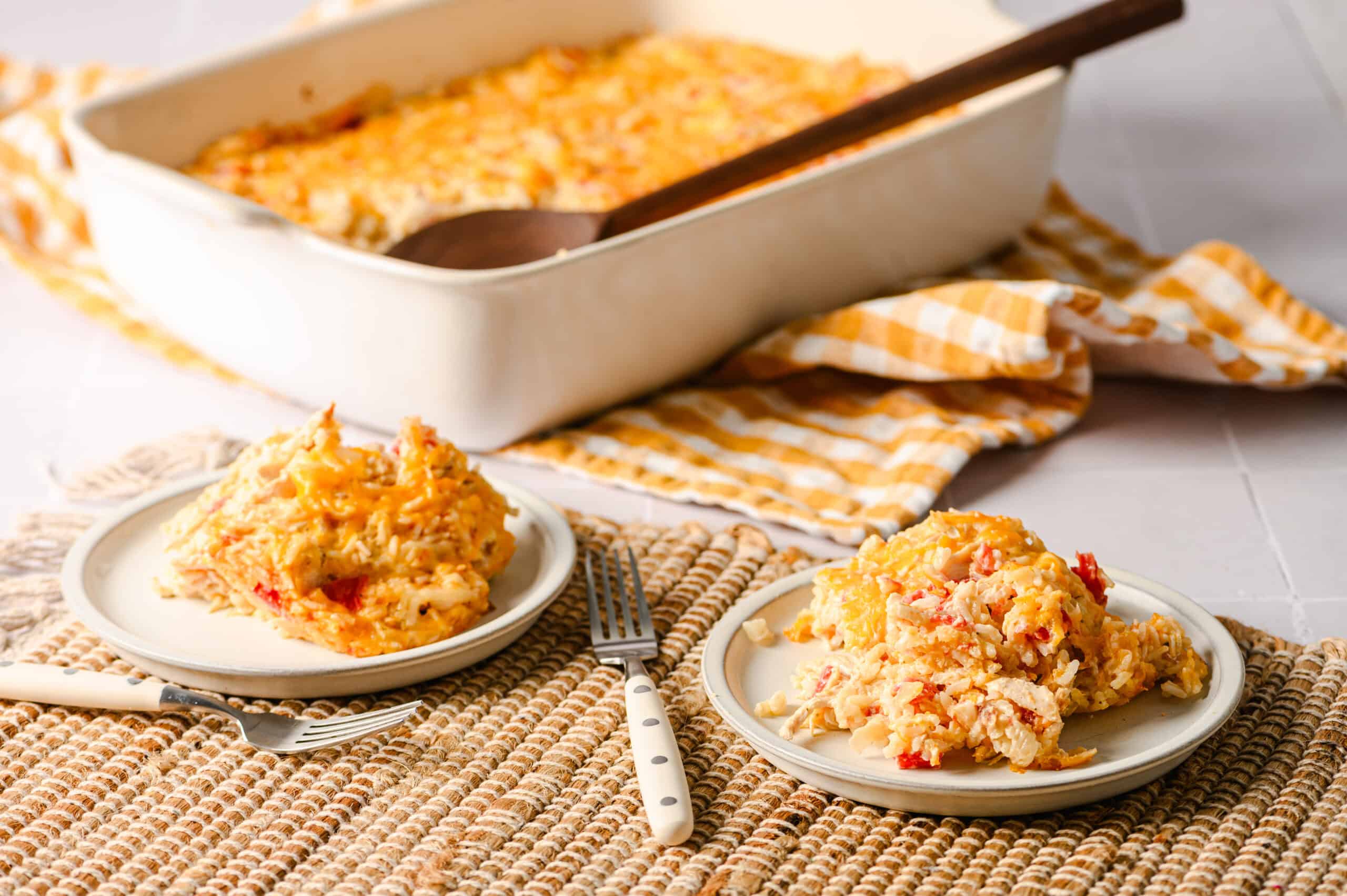 Creamy chicken casserole topped with melted cheese, served on white plates with a fork, set on a textured placemat in front of a baking dish of hot chicken casserole with a wooden spoon, featuring a cozy, home-cooked meal perfect for family dinner.