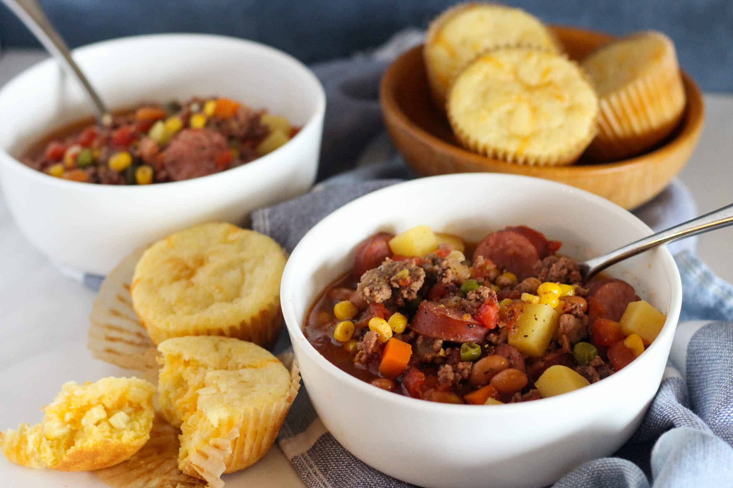 Savory beef chili soup in white bowls with cornbread muffins on a rustic table, perfect for comforting meals and meal prep. Classic chili with ground beef, beans, vegetables, served with fresh baked cornbread.