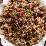 Savory wild rice salad with dried cranberries and pecans in a white serving dish.