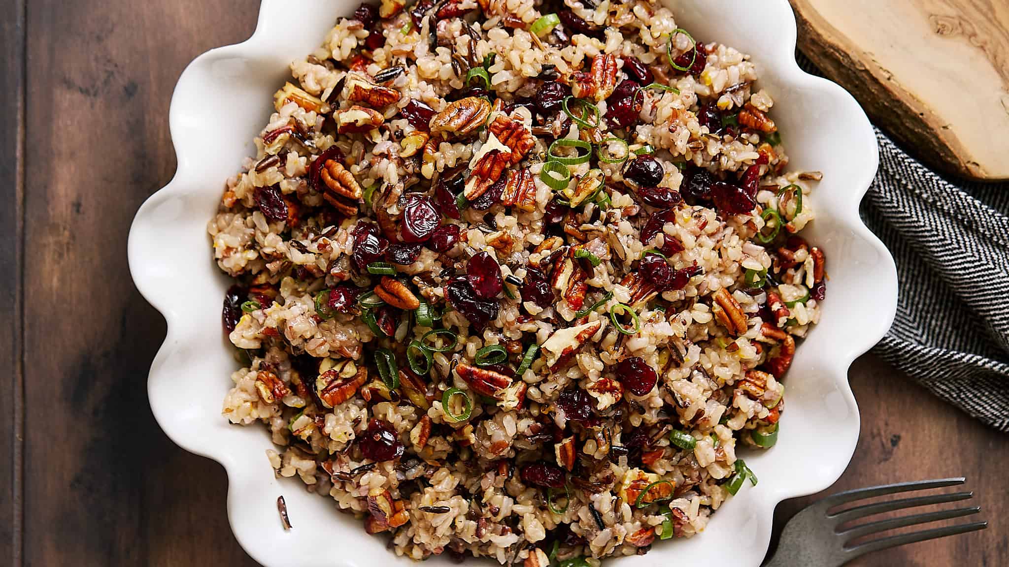 Savory wild rice salad with dried cranberries and pecans in a white serving dish.