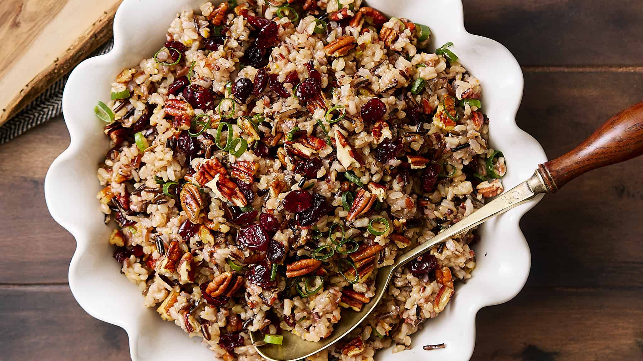 Savory wild rice salad with pecans, dried cranberries, and chopped green onions in a white serving dish. Perfect for healthy eating and holiday meals, packed with flavors and textures.