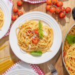 Savory spaghetti with cherry tomatoes, fresh basil, and Parmesan cheese served on white plates with a wooden table background.