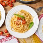 Savory spaghetti pasta with cherry tomatoes, fresh basil leaves, and shaved Parmesan cheese served on white plates for a delicious Italian meal.