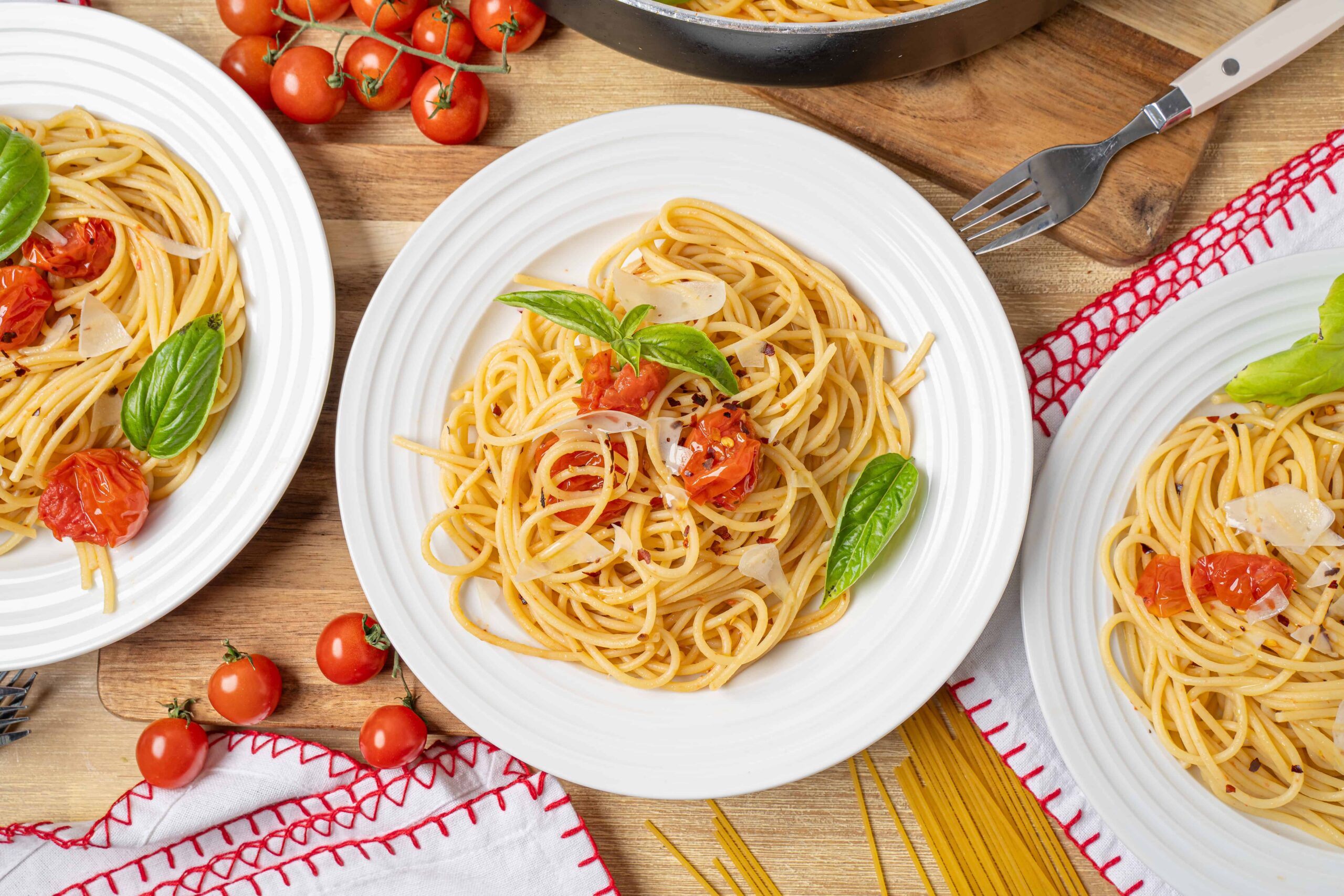Savory spaghetti pasta with cherry tomatoes, fresh basil leaves, and shaved Parmesan cheese served on white plates for a delicious Italian meal.