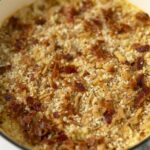 Golden baked casserole with bacon, cheese, and breadcrumbs in a green Dutch oven.