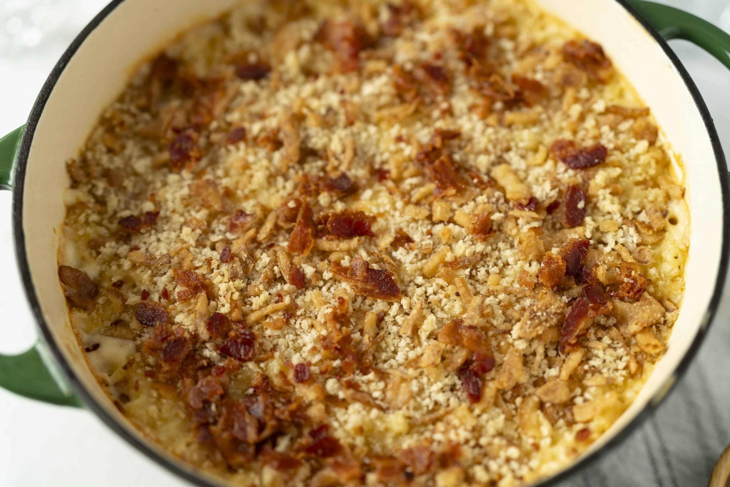 Golden baked casserole with bacon, cheese, and breadcrumbs in a green Dutch oven.