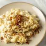 Creamy chicken casserole with crispy fried onions and breadcrumbs, served on a stylish beige plate, perfect for comforting home-cooked meals and family dinners.