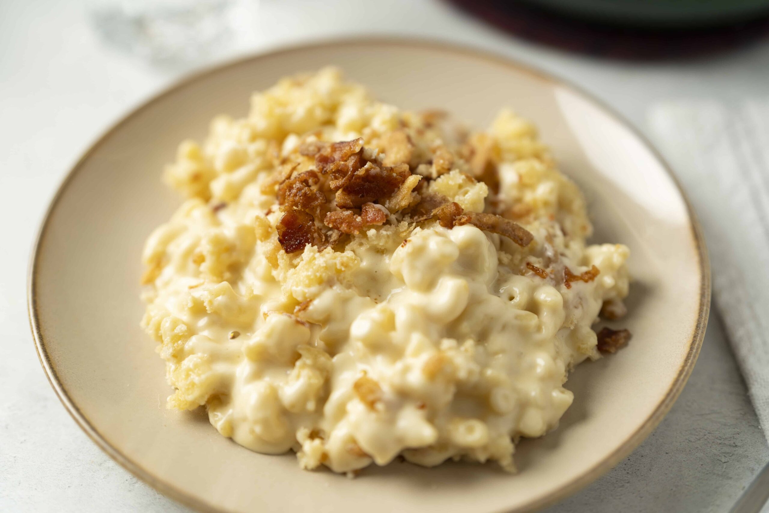 Creamy macaroni and cheese topped with crispy bacon bits served on a beige plate, perfect comfort food for dinner or lunch.