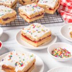 Delicious homemade strawberry shortcake bars with white frosting and colorful sprinkles on top. Perfect for dessert or special occasions. Ready to serve with fruit preserves and sweet toppings.
