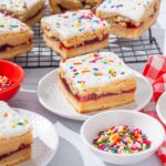 Bright, homemade sprinkle cake bars with white frosting and colorful sprinkles on white plates, served alongside bowls of sprinkles, perfect for festive dessert recipes or kids' parties.