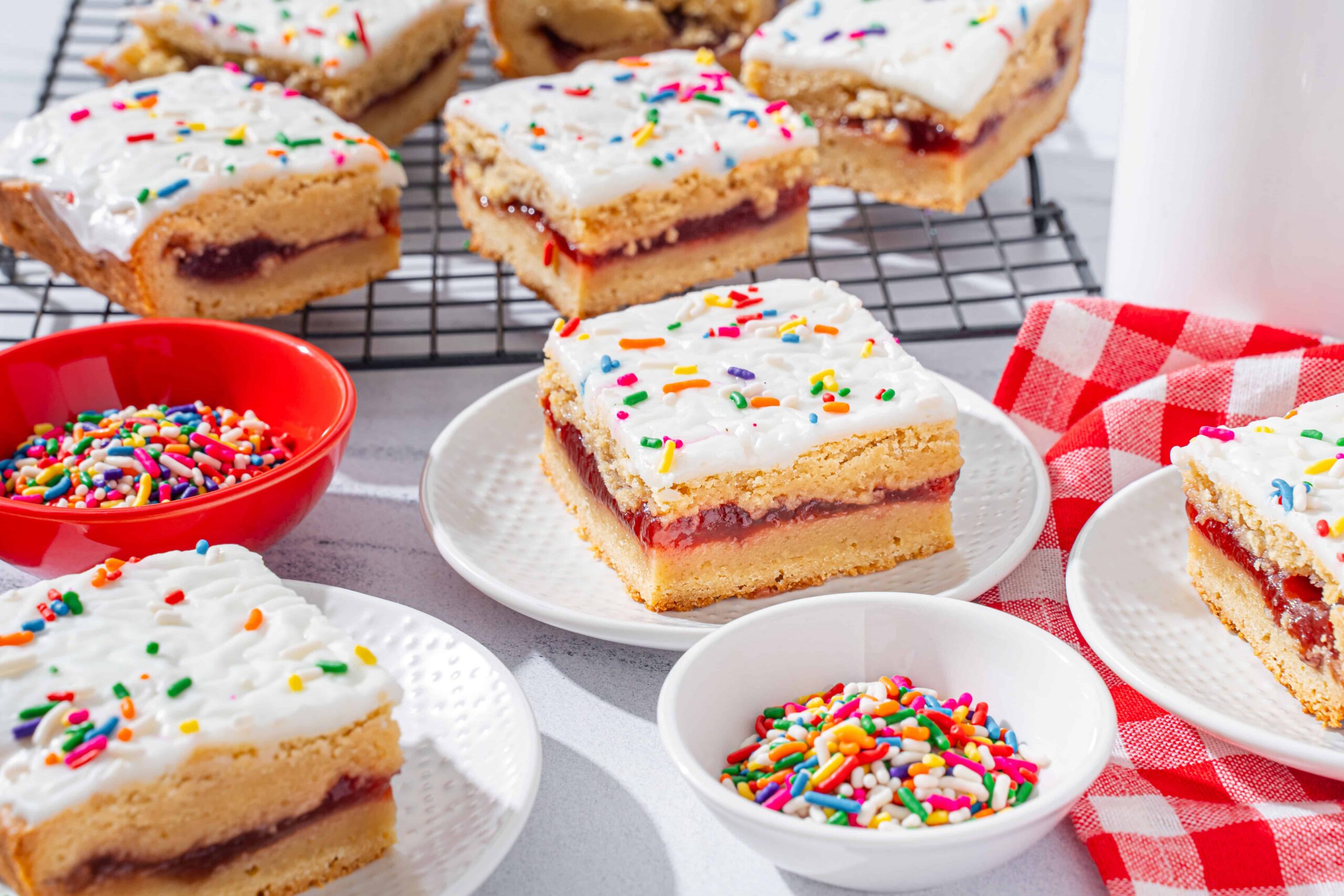 Bright, homemade sprinkle cake bars with white frosting and colorful sprinkles on white plates, served alongside bowls of sprinkles, perfect for festive dessert recipes or kids' parties.