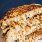 Crispy grilled cheese sandwich with melted cheese and tomato, close-up shot on a white plate.