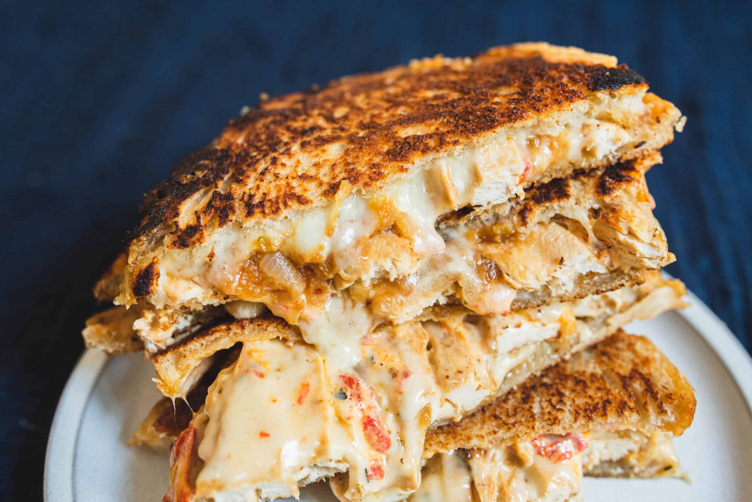 Crispy grilled cheese sandwich with melted cheese and tomato, close-up shot on a white plate.