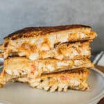 Crispy chicken grilled cheese sandwich with melted cheese and toasted bread on a beige plate.