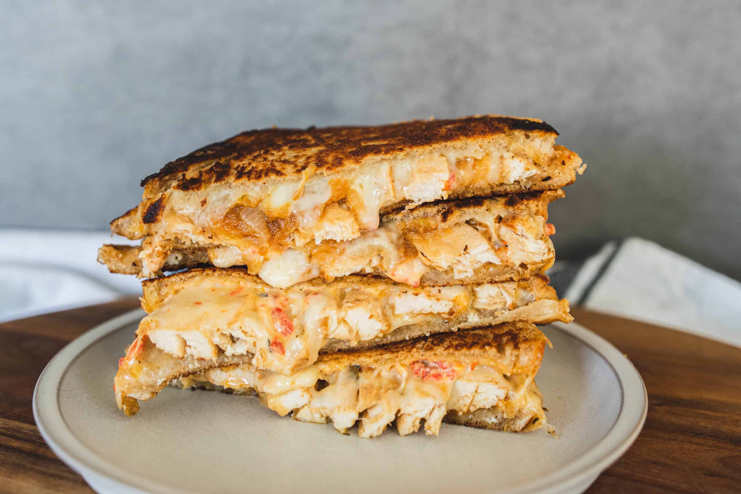 Crispy chicken grilled cheese sandwich with melted cheese and toasted bread on a beige plate.
