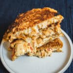Crispy chicken cordon bleu sandwich with melted cheese on a white plate, close-up, dark blue textured background.