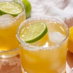 Refreshing lemon margarita cocktails with salt-rimmed glasses, lime slices, ice cubes, and fresh lemons on a wooden surface. Perfect for summer parties and citrus-flavored drinks.