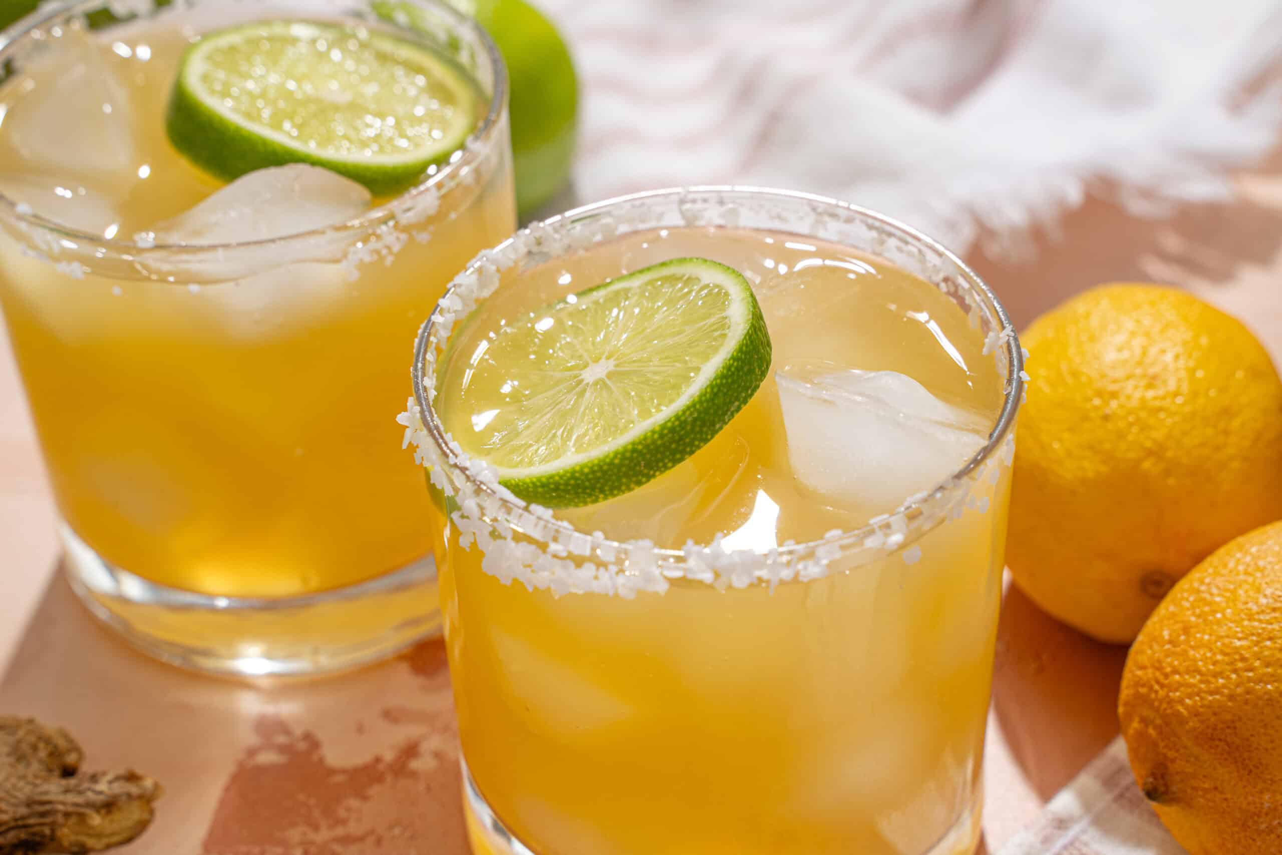 Refreshing lemon margarita cocktails with salt-rimmed glasses, lime slices, ice cubes, and fresh lemons on a wooden surface. Perfect for summer parties and citrus-flavored drinks.