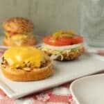 Cheeseburger sliders with melted cheese, fresh tomato, lettuce, pickles on sesame seed bun on white tray, delicious homemade mini cheeseburgers for lunch or dinner, tasty fast food meal, crispy and juicy patties, appetizing snack, savory American style burger, gourmet slider sandwiches, mouthwatering cheeseburger bites, popular comfort food, quick and easy to prepare.