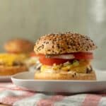 Golden sesame seed burger with fresh tomato, lettuce, cheese, and crispy bacon on a white plate. Perfect for casual lunch or delicious snack.