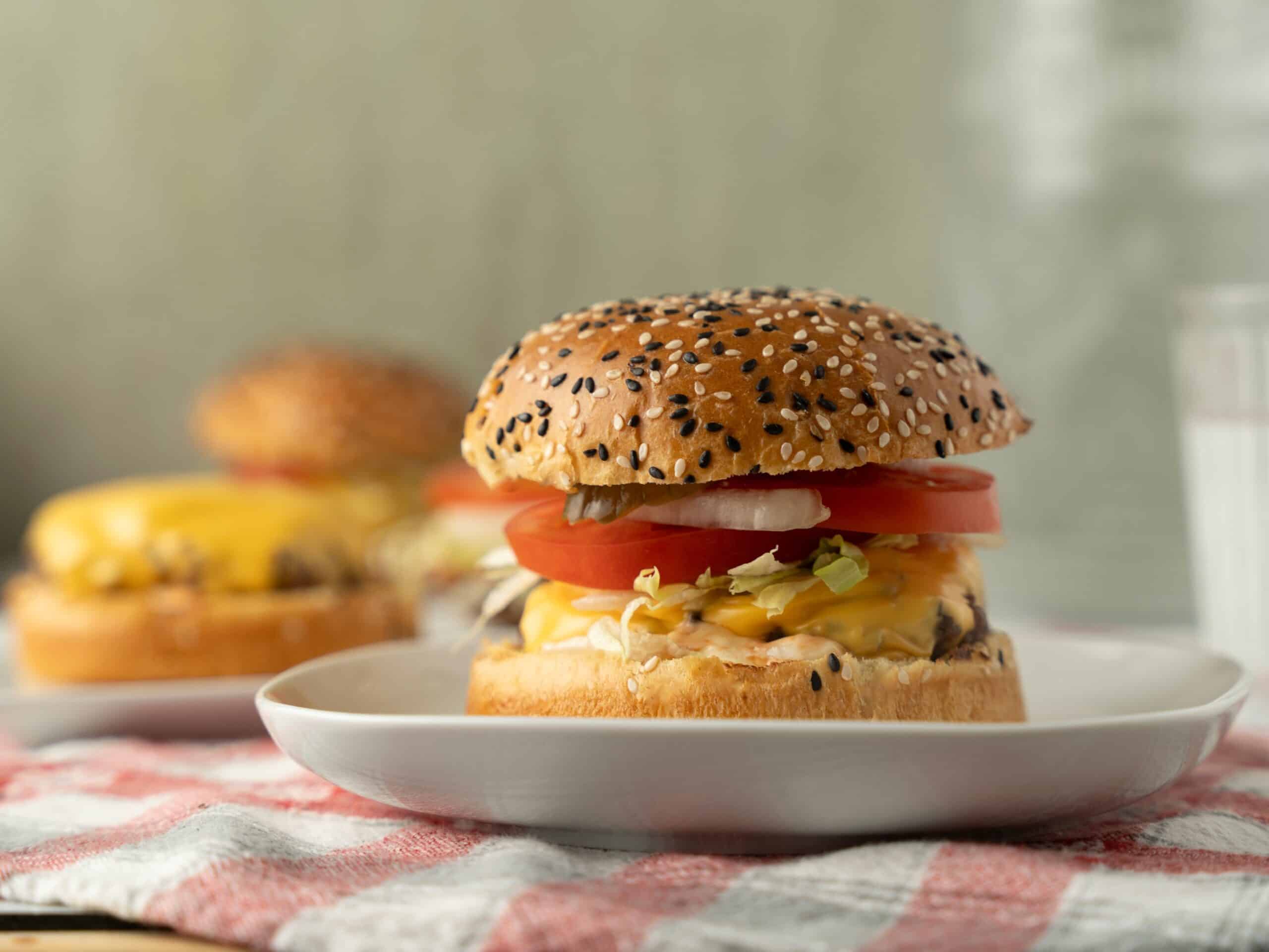 Golden sesame seed burger with fresh tomato, lettuce, cheese, and crispy bacon on a white plate. Perfect for casual lunch or delicious snack.