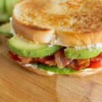 Crispy bacon and fresh avocado slices in a toasted bread sandwich on a wooden cutting board. Delicious homemade BLT sandwich with crispy bacon, ripe tomatoes, and creamy avocado.