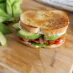 Fresh homemade BLT sandwich with crispy bacon, ripe tomato, creamy mayonnaise, crunchy lettuce, and sliced avocado on toasted bread on a wooden cutting board.