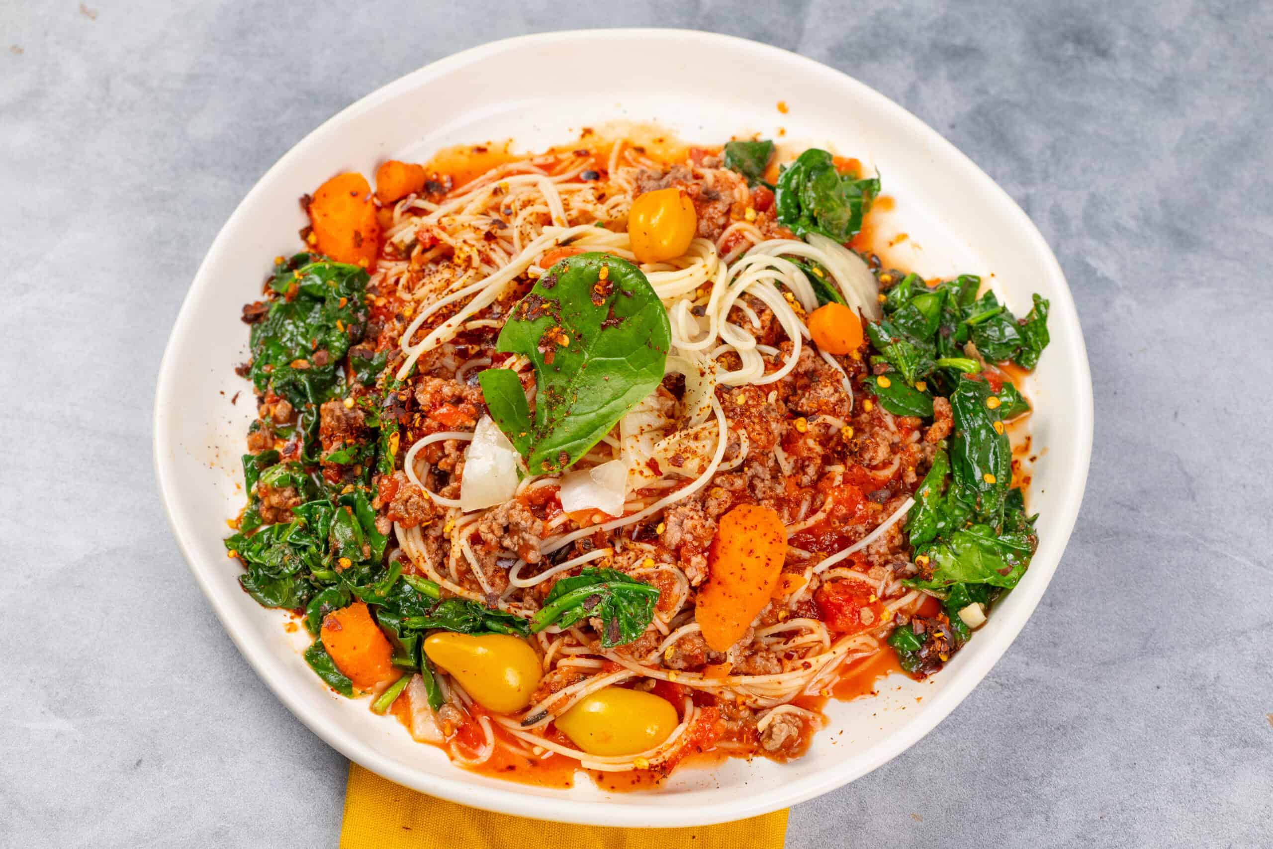 Savory spaghetti Bolognese with fresh basil, ground meat, vegetables, and rich tomato sauce on a white plate. Perfect for a hearty, flavorful Italian dinner.