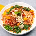 Spaghetti Bolognese with fresh vegetables and herbs on a white plate, served with a yellow napkin, showcasing a flavorful and colorful pasta dish.
