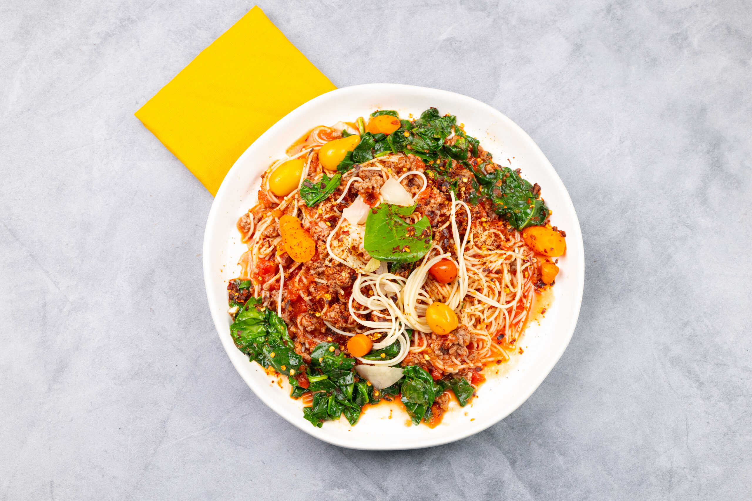 Sweet potato and beef pasta with kale, cherry tomatoes, and crunchy garlic breadcrumbs on a white plate.