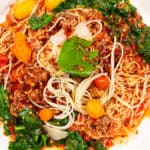Savory spaghetti bolognese with ground meat, vegetables, and herbs on a white plate, close-up shot.