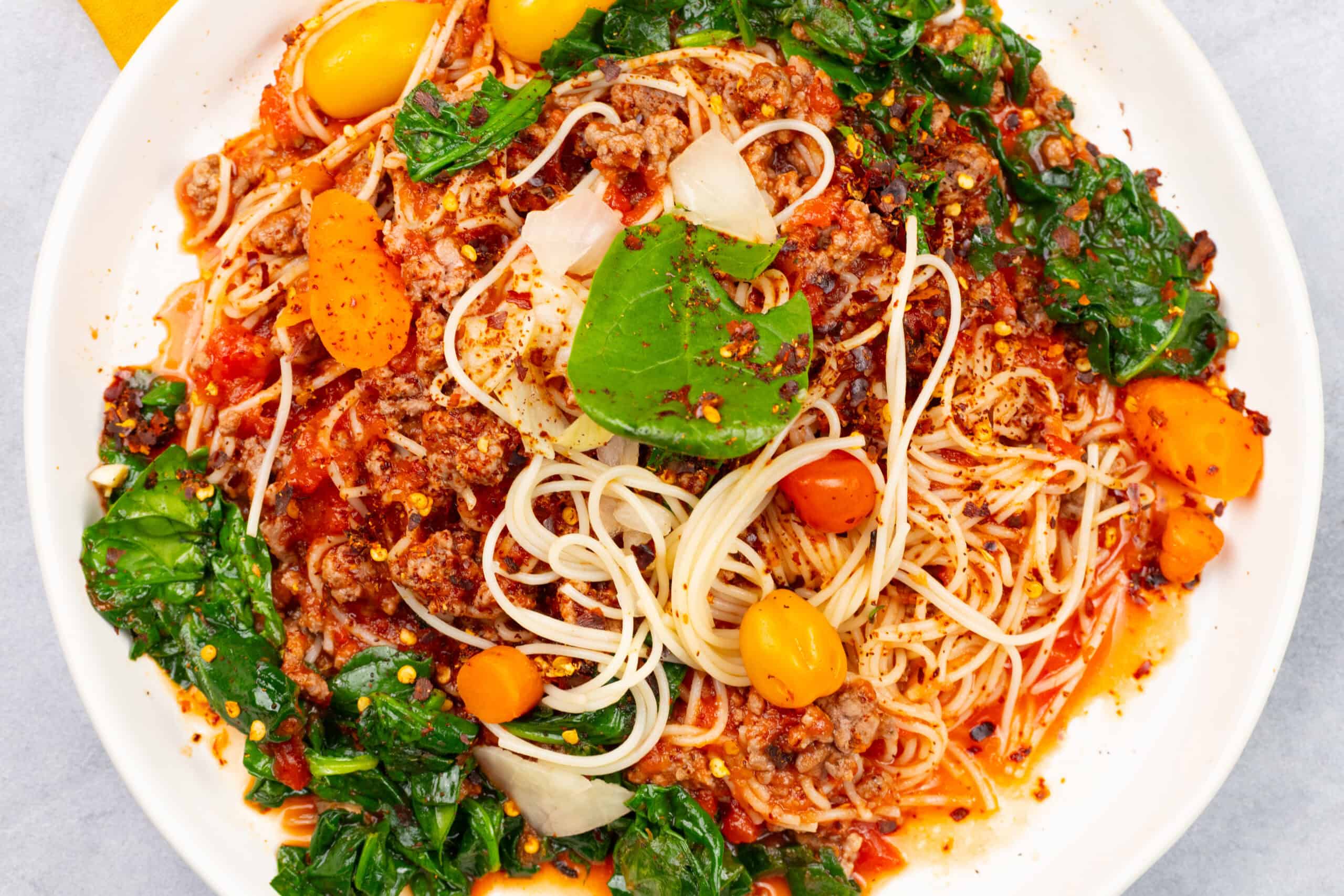 Savory spaghetti bolognese with ground meat, vegetables, and herbs on a white plate, close-up shot.