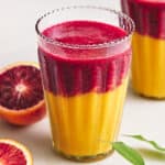 Vibrant blood orange and mango smoothies in tall glasses garnished with fresh blood orange slices, showcasing a colorful and refreshing fruit beverage.