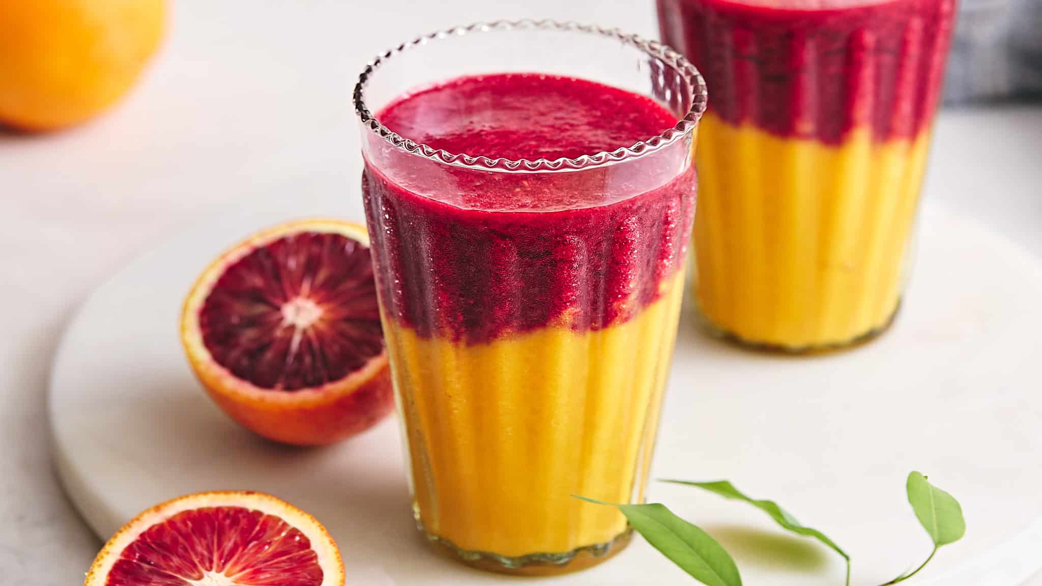 Vibrant blood orange and mango smoothies in tall glasses garnished with fresh blood orange slices, showcasing a colorful and refreshing fruit beverage.