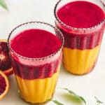 Fresh blood orange and mango smoothies served in tall glasses, garnished with blood orange slices, on a white plate. A vibrant, healthy smoothie recipe perfect for breakfast or summer refreshment.