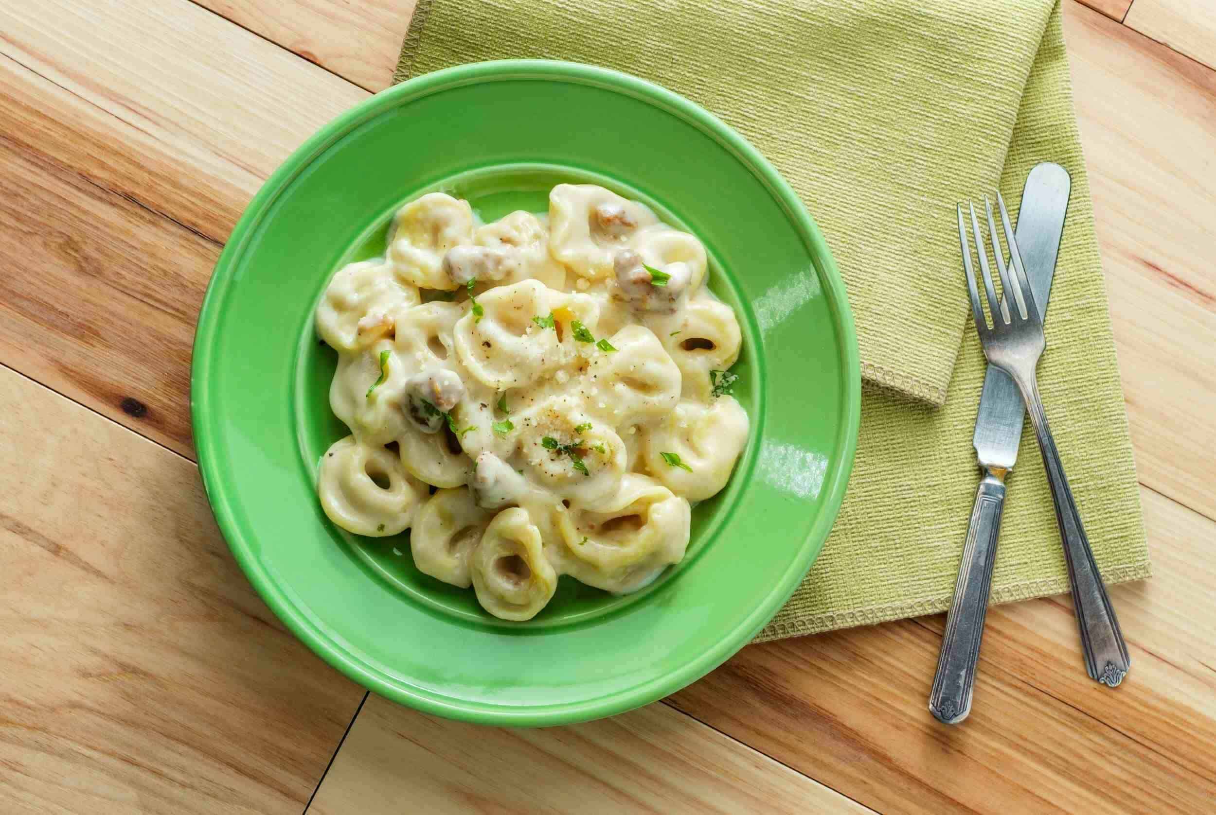 Creamy tortellini pasta with cheese and herbs served on a vibrant green plate, perfect for a comforting meal.