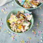 Colorful rainbow popcorn with sprinkles and drizzle in pastel colors served in green bowls on a textured gray surface.