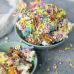 Colorful rainbow popcorn drizzled with vibrant frosting and rainbow sprinkles in two light blue bowls. Perfect sweet and crunchy snack for parties or movie nights, featuring pink, yellow, blue, and purple toppings.