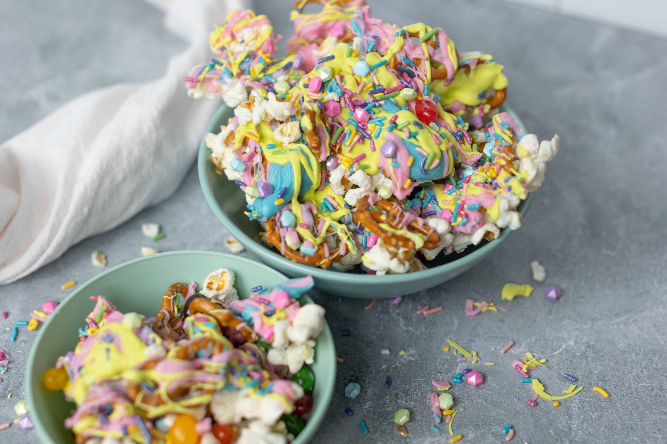 Colorful rainbow popcorn drizzled with vibrant frosting and rainbow sprinkles in two light blue bowls. Perfect sweet and crunchy snack for parties or movie nights, featuring pink, yellow, blue, and purple toppings.