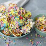 Colorful rainbow popcorn with sprinkles, drizzled with pastel-colored candy coatings, served in light teal bowls, perfect for fun snacks or birthday treats.
