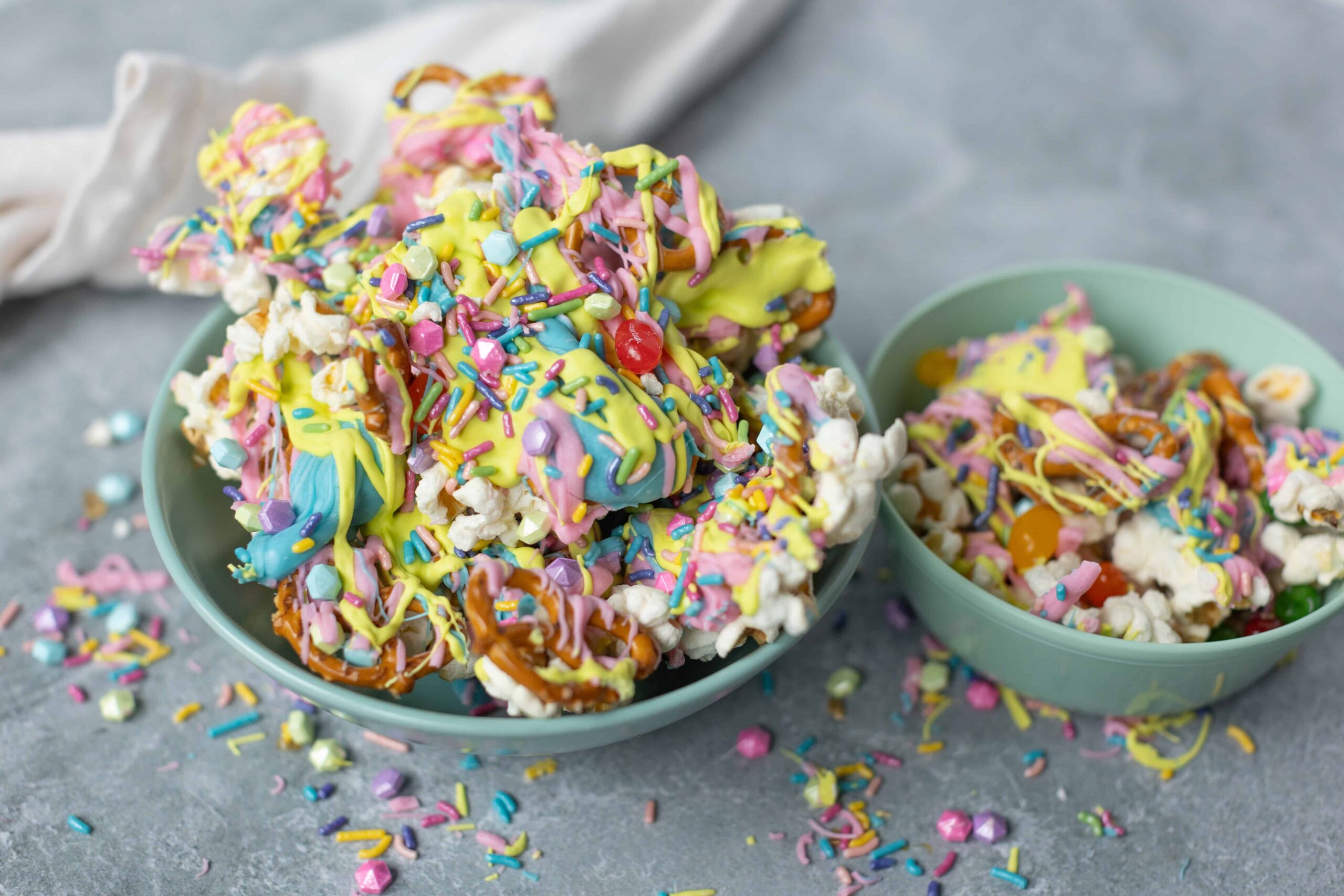 Colorful rainbow popcorn with sprinkles, drizzled with pastel-colored candy coatings, served in light teal bowls, perfect for fun snacks or birthday treats.