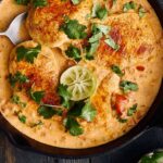 Juicy chicken cooked in creamy peanut sauce garnished with cilantro and lime slices in a cast iron skillet.