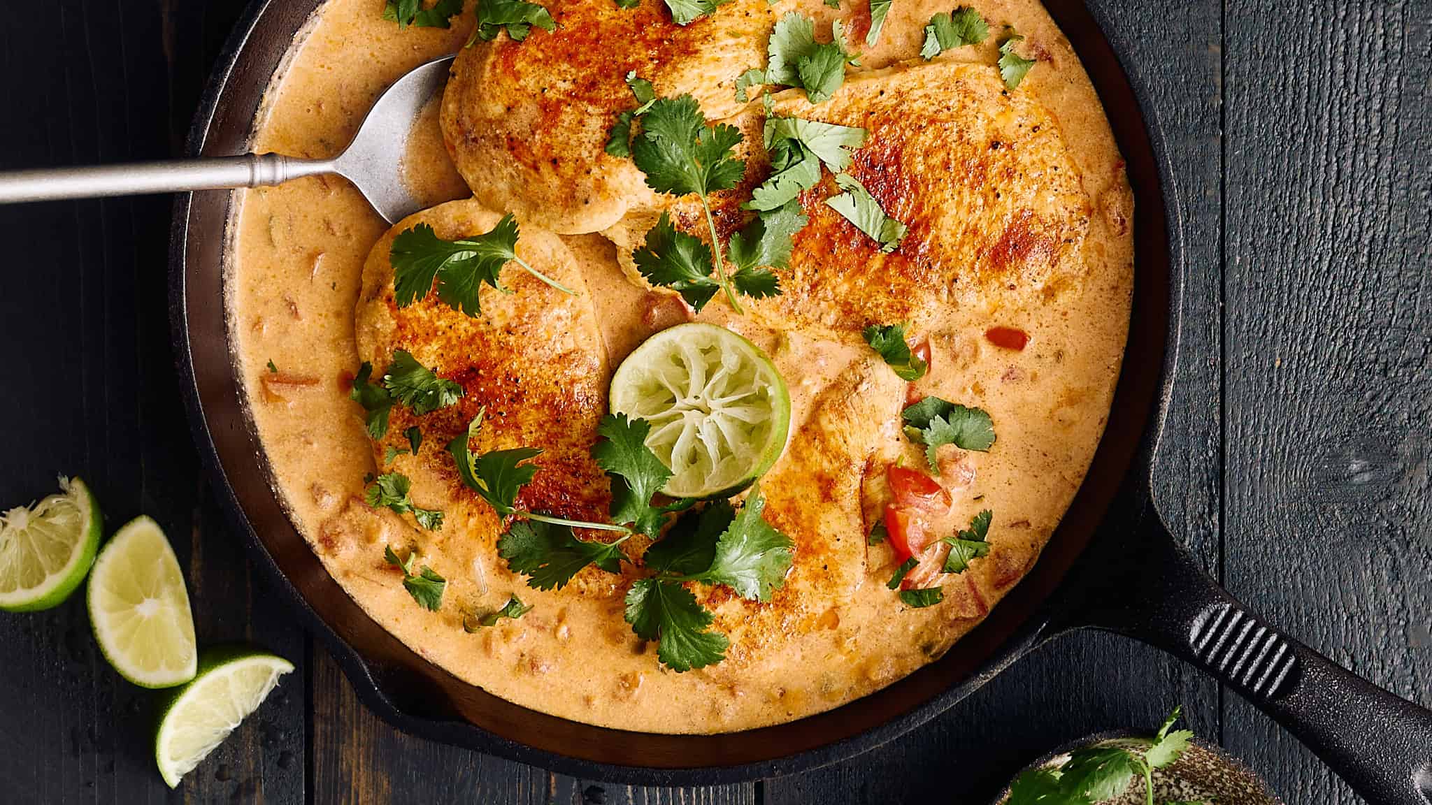 Juicy chicken cooked in creamy peanut sauce garnished with cilantro and lime slices in a cast iron skillet.