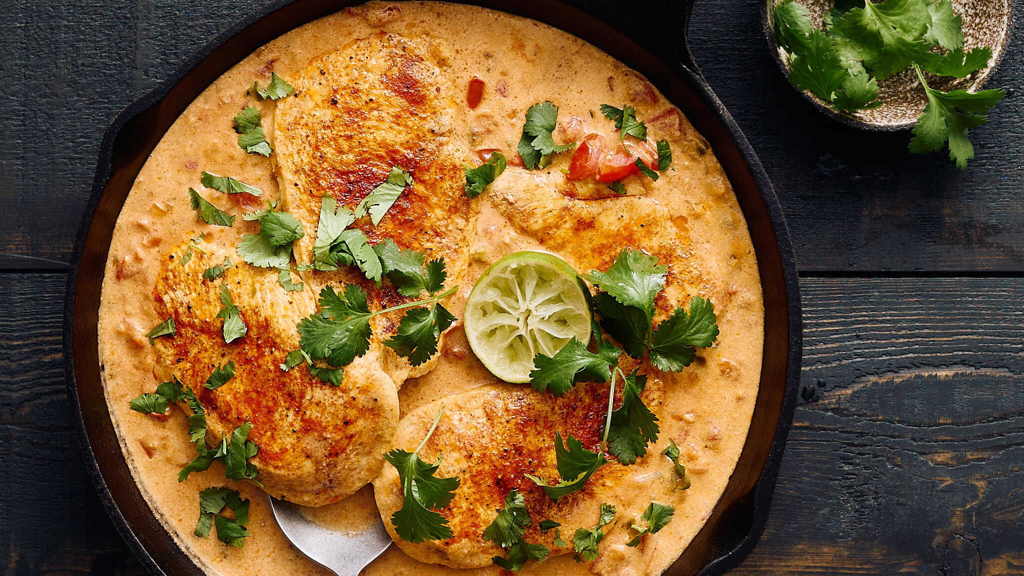 Juicy chicken breasts in creamy cilantro-lime sauce garnished with fresh cilantro and lime slices in a rustic cast iron skillet.
