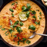 Juicy chicken in rich creamy sauce garnished with cilantro and lime wedges in a cast iron skillet. Perfect for flavorful, hearty dinner recipes.