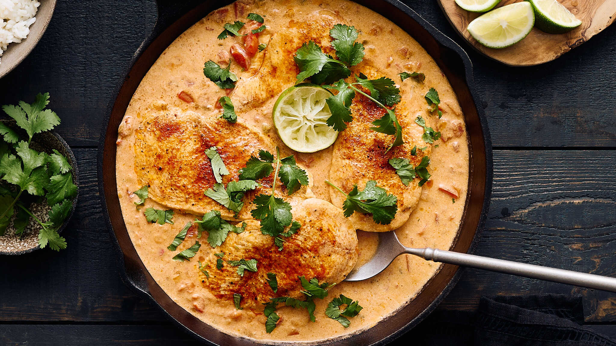 Juicy chicken in rich creamy sauce garnished with cilantro and lime wedges in a cast iron skillet. Perfect for flavorful, hearty dinner recipes.