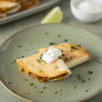 Crispy beef burrito with melted cheese and sour cream on a green plate.