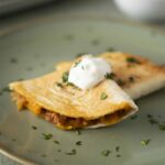 Savory breakfast quesadilla with melted cheese, beans, and sour cream on a green plate.