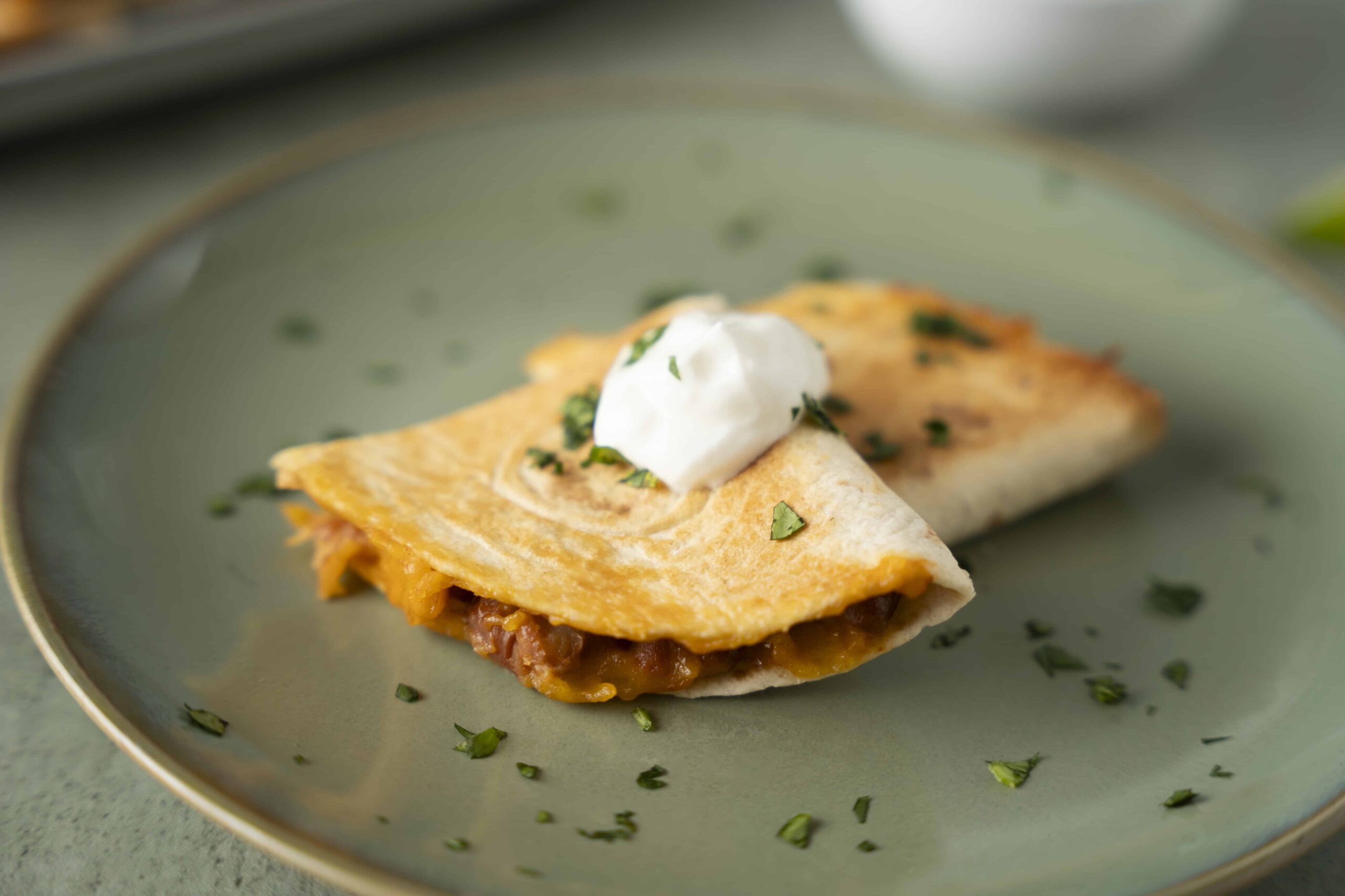 Savory breakfast quesadilla with melted cheese, beans, and sour cream on a green plate.