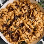 Creamy skillet pasta with caramelized onions and herbs, served in a white dish in a rustic setting.